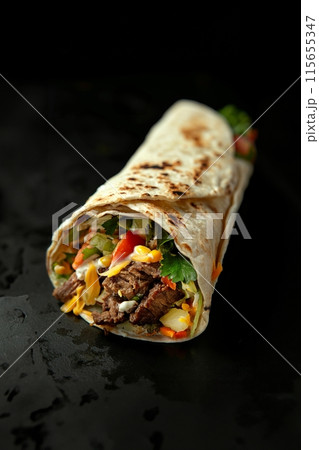 Juicy beef shawarma wrap bursting with fresh veggies on a sleek black slate 115655347