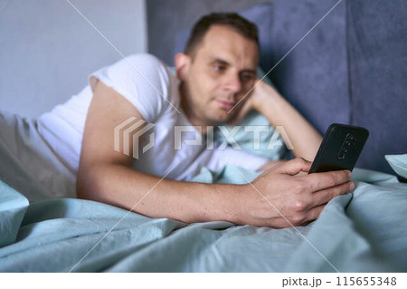 a young man scrolls in smartphone in the morning after waking up, morning routine 115655348