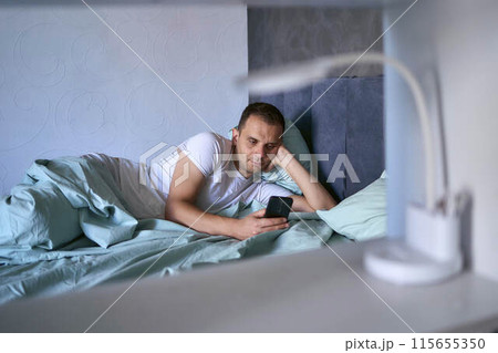 a young man scrolls in smartphone in the morning after waking up, morning routine 115655350