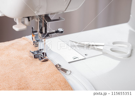 Modern sewing machine special presser foot with beige velveteen fabric and zipper, closeup 115655351