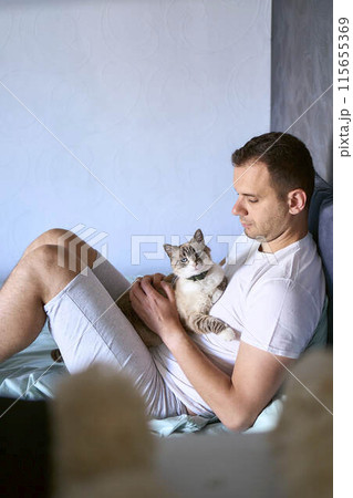 a  young man pet a cat in bed, morning routine 115655369