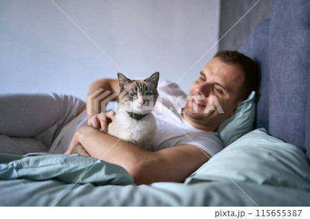 a  young man pet a cat in bed, morning routine 115655387