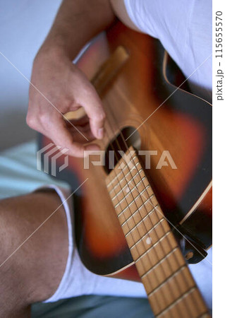 a young man is learning to play the guitar at home, a cat is lying next to him and listening a young man is learning to play the guitar at home, a cat is lying next to him and listening 115655570