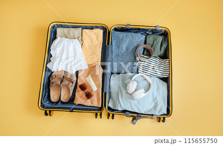 suitcase with clothes for traveling on a yellow background. Vacation and leisure concept, business trip. Flat lay, top view 115655750