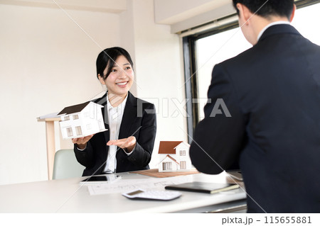 住宅模型を使い提案するスーツ姿の若い女性 115655881