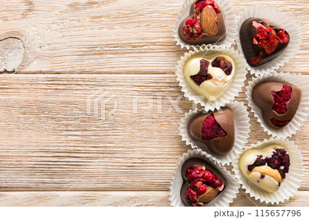 chocolate sweets in the form of a heart with fruits and nuts on a colored background. top view with space for text, holiday concept chocolate sweets in the form of a heart with fruits and nuts on a colored background. top view with space for text, holiday concept 115657796