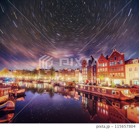 Beautiful night in Amsterdam. Night illumination of buildings and boats near the water in the canal. 115657804