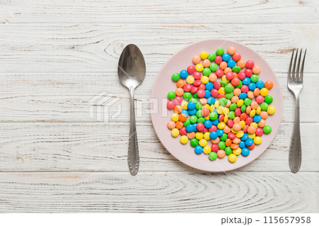cutlery on table and sweet plate of candy. Health and obesity concept, top view on colored background 115657958