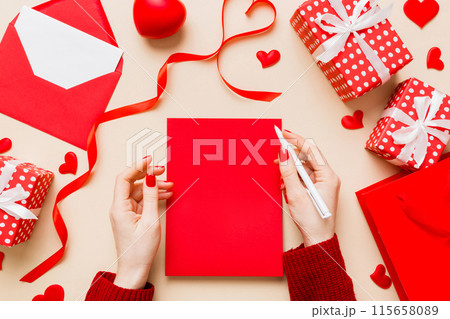 top view photo of valentine day decor female hands holding letter with envelope, small gift box and heart decoration on isolated pastel colored background with empty space 115658089