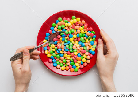 the girl holds cutlery in her hands and eats sweets in a plate. Health and obesity concept, top view on colored background 115658090