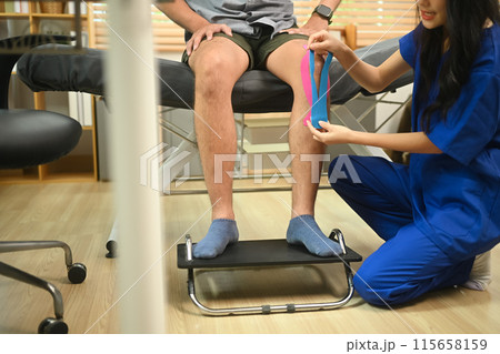 Physiotherapist applying elastic kinesiology tape on patient knee. Sport physical therapy concept Physiotherapist applying elastic kinesiology tape on patient knee. Sport physical therapy concept 115658159