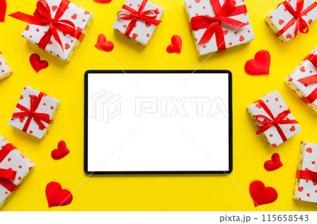 Top view of digital tablet with gift boxes and hearts on colorful background. Tablet with black screen with Holiday decorations gift box top view 115658543