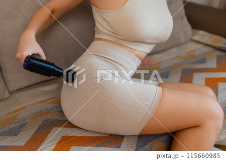 Gun shock vibration percussion massage therapy. Sporty woman practicing self-massaging your legs close up. Applying therapeutic percussive massage gun in living room at home indoors. Copy text space Gun shock vibration percussion massage therapy. Sporty woman practicing self-massaging your legs close up. Applying therapeutic percussive massage gun in living room at home indoors. Copy text space 115660985