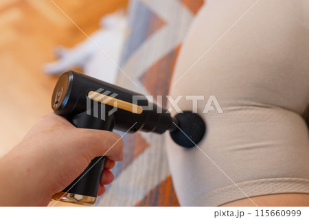 Gun shock vibration percussion massage therapy. Sporty woman practicing self-massaging your legs close up. Applying therapeutic percussive massage gun in living room at home indoors. Copy text space Gun shock vibration percussion massage therapy. Sporty woman practicing self-massaging your legs close up. Applying therapeutic percussive massage gun in living room at home indoors. Copy text space 115660999