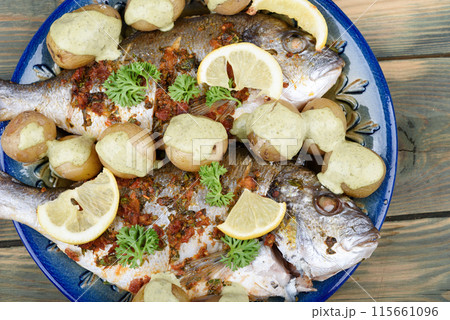Baked dorado fish and baby potatoes on a plate with gremolata seasoning and cream sauce. Baked dorado fish and baby potatoes on a plate with gremolata seasoning and cream sauce. 115661096