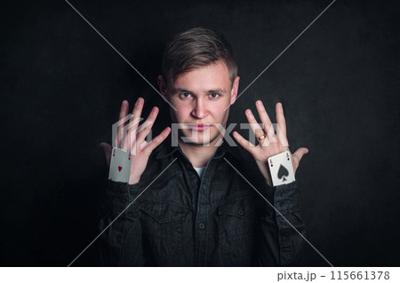 Confident tricky gambler with aces up sleeves. Illusionist showing tricks with playing cards isolated on dark background. Gambling games, luck and delusion concept 115661378