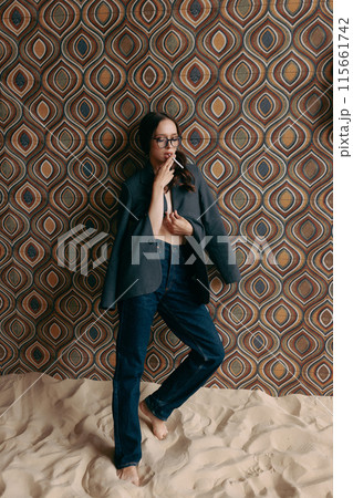Woman in an unbuttoned jacket and jeans posing against a wall 115661742