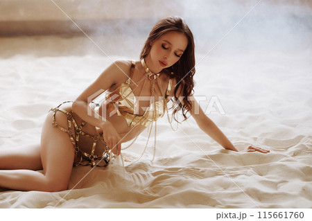 A woman is laying on the sand in a bikini, with a chain around her waist 115661760