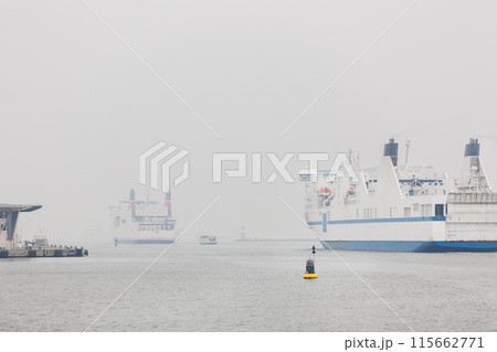 Big modern ferry ship navigate from Rostock harbor Warnemunde bay foggy spring autumn morning misty weather scenic view background. Maritime traffic liner passenger cargo vessel at Baltic sea Germany 115662771