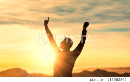 Success, achieving goals in business and life, feeling of triumph. , symbol of achievement. silhouette of man on top of mountain with his arms raised in triumph at sunset, joy and satisfaction 115662862