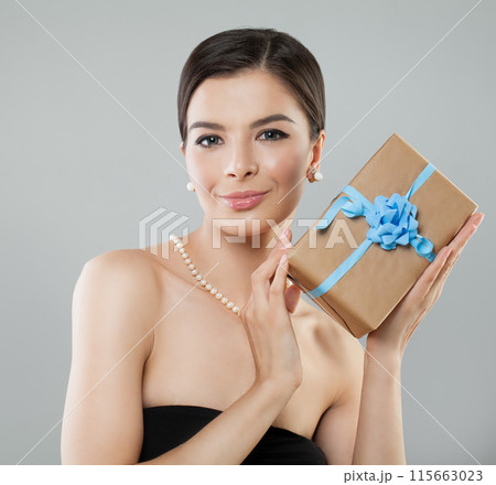 Happy pretty brunette lady female model showing gift box over grey background. Happy pretty brunette lady female model showing gift box over grey background. 115663023