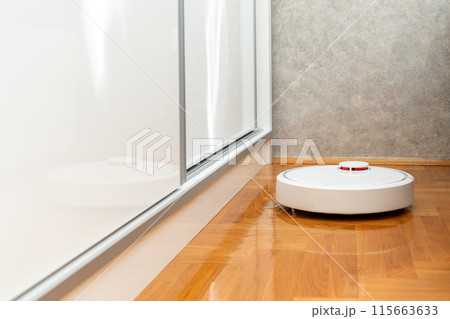 White robot vacuum cleaner on the wooden floor in bedroom. Cleaning the apartment with a modern smart vacuum cleaner White robot vacuum cleaner on the wooden floor in bedroom. Cleaning the apartment with a modern smart vacuum cleaner 115663633