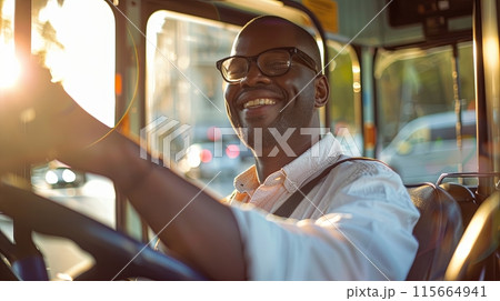 a cheerful young man with glasses, smiling brightly as he sits behind the wheel of a tram 115664941