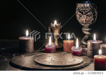 An eerie occult ritual setup featuring lit candles, a mystical symbol on slate, and a ceremonial goblet in a dark, moody setting. An eerie occult ritual setup featuring lit candles, a mystical symbol on slate, and a ceremonial goblet in a dark, moody setting. 115665015