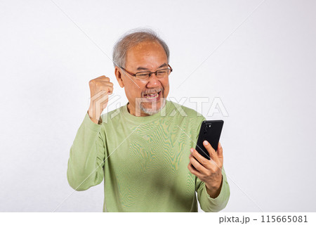 Portrait Asian smiling old man holding a cell phone celebrating something on the phone studio shot isolated on white background, happy senior man doing winner gesture celebrate on mobile phone Portrait Asian smiling old man holding a cell phone celebrating something on the phone studio shot isolated on white background, happy senior man doing winner gesture celebrate on mobile phone 115665081