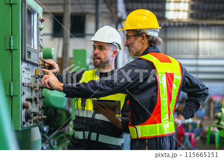 Two men in safety gear are working on a machine 115665151