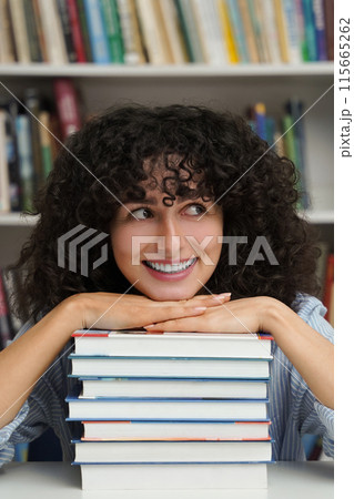 Female student with stack of books sitting at table in library Female student with stack of books sitting at table in library 115665262