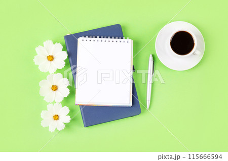 Composition with opened blank notepad and pen, cup of black coffee, flowers of a white cosmos on a green background. Festive office desktop concept. Morning coffee cup. Composition with opened blank notepad and pen, cup of black coffee, flowers of a white cosmos on a green background. Festive office desktop concept. Morning coffee cup. 115666594