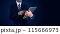 Businessman in a suit using a tablet, standing against a dark background. Ideal for business, technology, and professional concept 115666973
