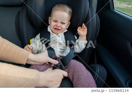 Crying toddler girl sitting in safety car seat. Baby is sad, upset and scared 115668114