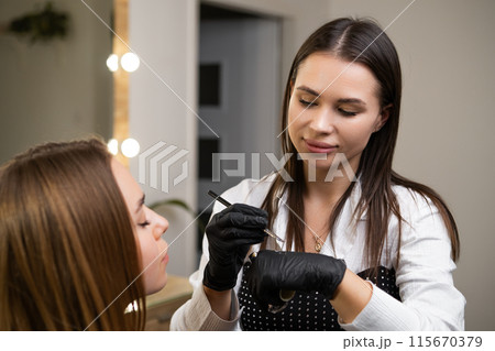 A beautician performs a brow lamination procedure on a client at beauty salon 115670379