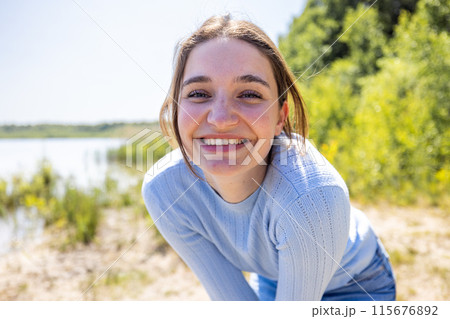A beautiful brunette woman smiling happily outdoors by a bright lakeside on a sunny day in nature 115676892