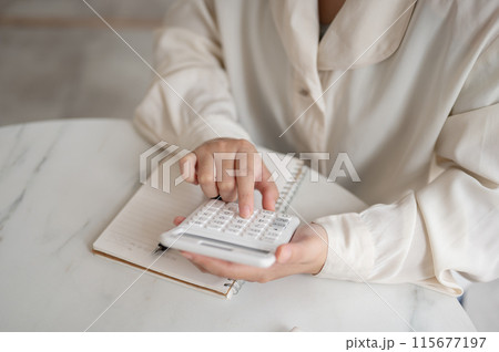 A close-up image of a woman using a calculator at a table, checking and calculating her budget. A close-up image of a woman using a calculator at a table, checking and calculating her budget. 115677197