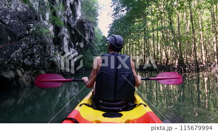 Tourist in kayak holds paddle pointing with hand at cliff Tourist in kayak holds paddle pointing with hand at cliff 115679994