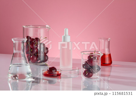 The pink background photo was taken from a diagonal angle. Beakers containing fresh cherry, transparent and red liquid erlenmeyer flask, all surround a blank cosmetic bottle in center, blank space 115681531