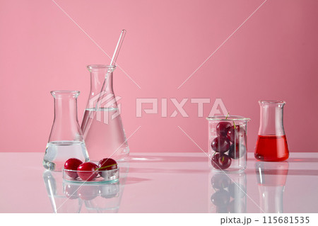 White table contains some erlenmeyer flask of transparent liquid on the left, a beaker of fresh cherry fruit and red liquid erlenmeyer flask on the right, vacant space in center for product displaying White table contains some erlenmeyer flask of transparent liquid on the left, a beaker of fresh cherry fruit and red liquid erlenmeyer flask on the right, vacant space in center for product displaying 115681535