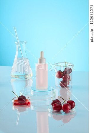 An unlabeled cosmetic bottle displayed on two glass podiums stack of each others, around it is a transparent fluid erlenmeyer flask, a dish of red liquid, petri dish and beaker contains ripe cherries An unlabeled cosmetic bottle displayed on two glass podiums stack of each others, around it is a transparent fluid erlenmeyer flask, a dish of red liquid, petri dish and beaker contains ripe cherries 115681575