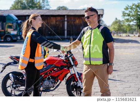 Motorcycle driving school concept. Male instructor and happy female student handshake before start of the classes. Safe ride lessons for motorcycle driving. Motorcycle driving school concept. Male instructor and happy female student handshake before start of the classes. Safe ride lessons for motorcycle driving. 115681621