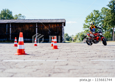 L-driver female driver with helmet taking motorcycle lessons and practicing ride. slalom through the orange cones on motordrome on motorcycle. Motorcycle school of driving. 115681744
