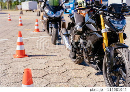 A motorcycle is parked in front of a row of orange cones. The motorcycle is black and yellow. Concept of motorcycle school of driving A motorcycle is parked in front of a row of orange cones. The motorcycle is black and yellow. Concept of motorcycle school of driving 115681943