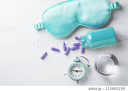 Turquoise sleeping mask, pill capsules, glass of water alarm clock on white table background, top view, copy space 115682238