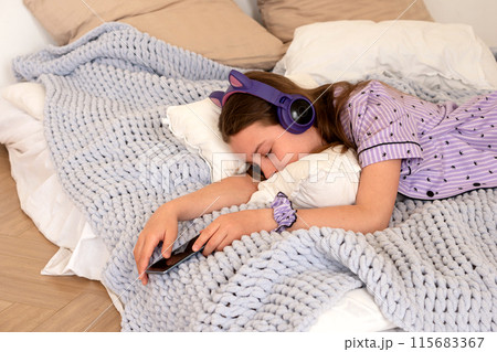 Teenage girl asleep in bed with headphones and smartphone. 115683367