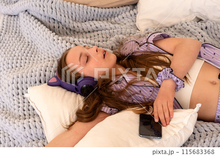 Teenage girl asleep in bed with headphones and smartphone. 115683368