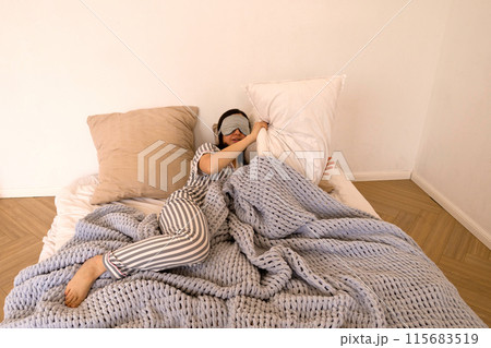 Woman lying in bed covering eyes with eye mask. Woman lying in bed covering eyes with eye mask. 115683519