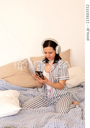 Woman reacting to smartphone content with headphones in bed. 115683552
