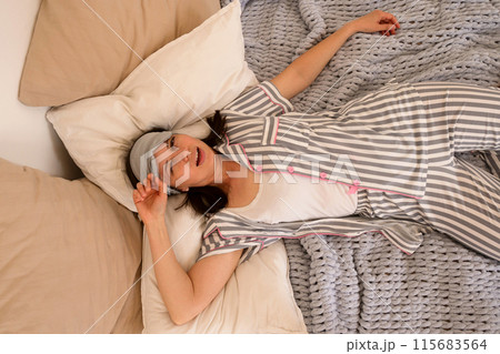Woman laughing while lying in bed, wearing eye mask. Woman laughing while lying in bed, wearing eye mask. 115683564